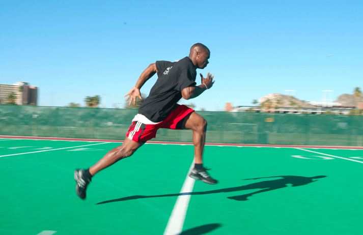 A man in a black shirt and red shorts is running on a green field.