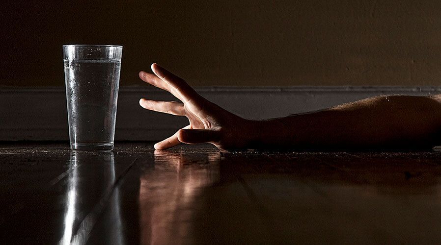 A hand is reaching for a glass of water on the floor.