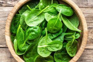 A wooden bowl filled with spinach leaves on a wooden table.