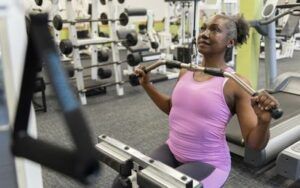 An older woman is using a lat pulldown machine in a gym.