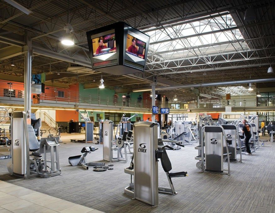 A gym with a lot of exercise equipment and a tv hanging from the ceiling