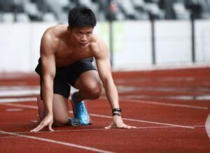 A shirtless man is getting ready to run on a track.