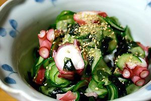 A white bowl filled with a salad of cucumbers , octopus , and sesame seeds.