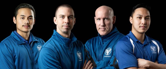 Four men in blue jackets are standing next to each other with their arms crossed.