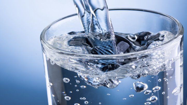 Water is being poured into a glass on a blue background.