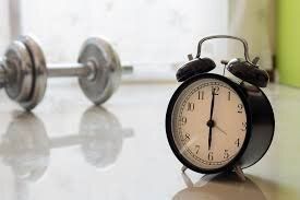 An alarm clock is sitting on a table next to a pair of dumbbells.