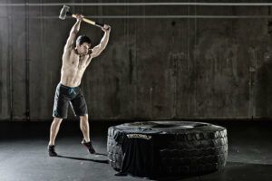 A shirtless man is holding a hammer over a tire.