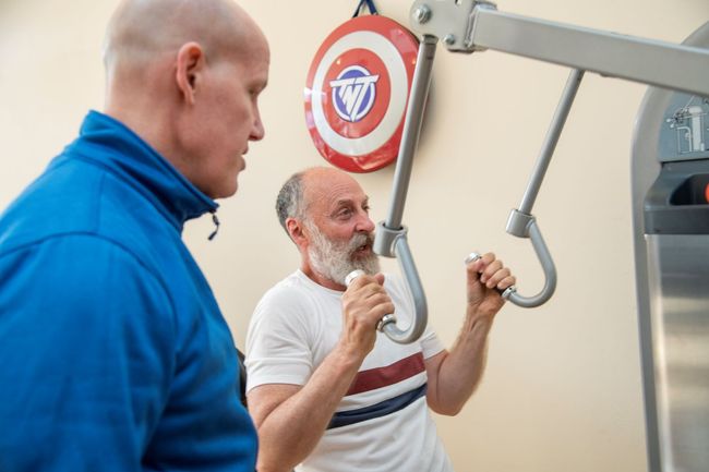 Two men are working out on a machine in a gym.