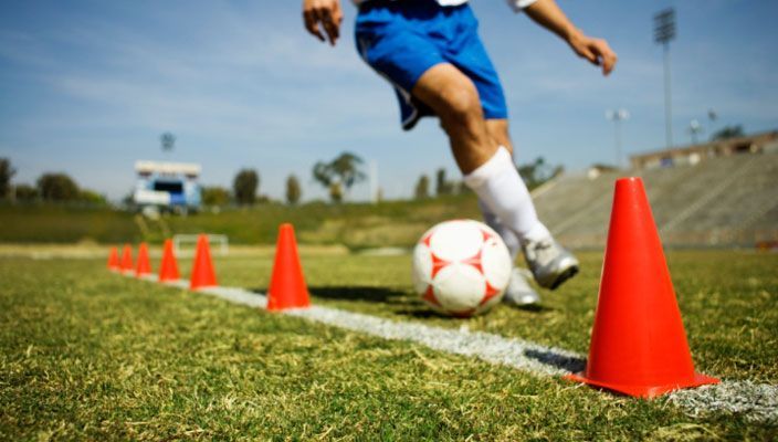 A soccer player is kicking a soccer ball between red cones on a field.