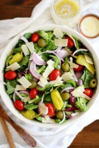 A salad with tomatoes , olives , peppers , onions and parmesan cheese in a bowl on a table.