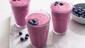 Three glasses of blueberry smoothies with blueberries on top on a table.