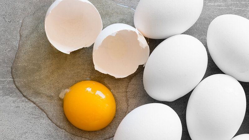 A broken egg is sitting on top of a pile of white eggs.