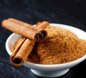 Cinnamon sticks are sitting on top of a bowl of cinnamon powder.