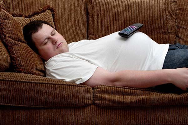 A man is laying on a couch with a remote control on his belly.