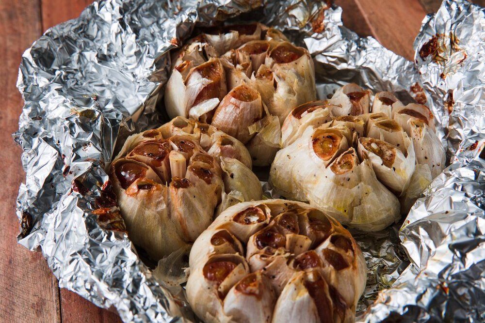 The garlic is sitting on a piece of tin foil on a wooden table.