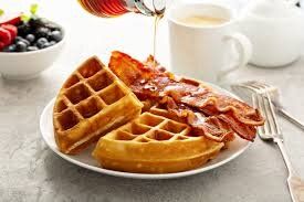 There is a plate of waffles with bacon and syrup on it.