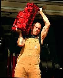 A man in overalls is holding a red box over his head.