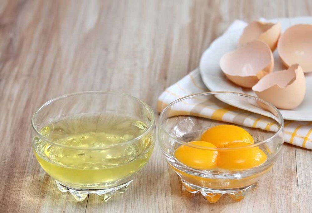 There are two bowls of eggs on a wooden table.