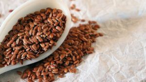 A white spoon filled with flax seeds on a table.