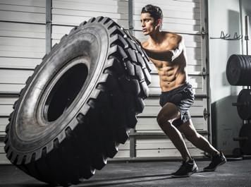 A man is flipping a tire in a gym.