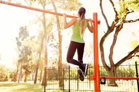 A woman is doing pull ups on a bar in a park.