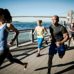 A group of people are running on a sidewalk near the water.