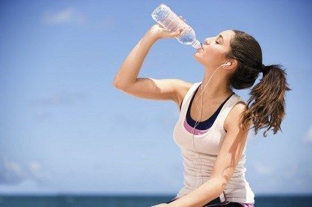 A woman is drinking water from a bottle on the beach.