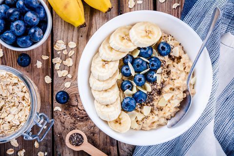 A bowl of oatmeal with bananas and blueberries on a wooden table.