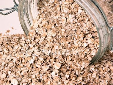 Oats are pouring out of a glass jar on a table.