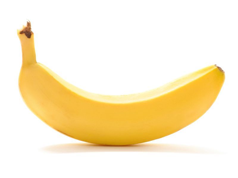 A single banana is sitting on a white surface.