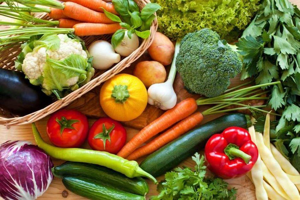 A variety of fresh vegetables are sitting on a wooden table.