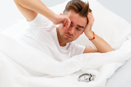 A man is laying in bed looking at an alarm clock.