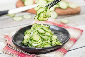 A person is picking up sliced cucumbers from a bowl with chopsticks.