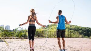 A man and a woman are jumping rope in a park.