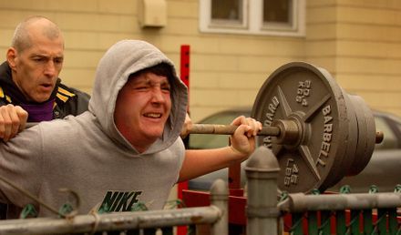 A man in a nike shirt is squatting with a barbell.