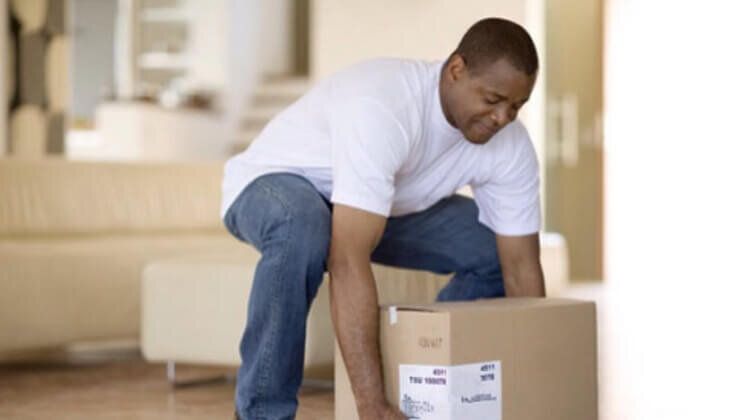 A man is lifting a cardboard box in a living room.