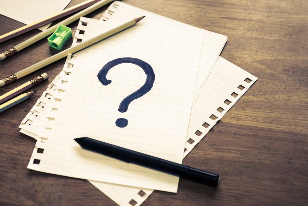 A question mark is drawn on a piece of paper next to a pen and pencils.