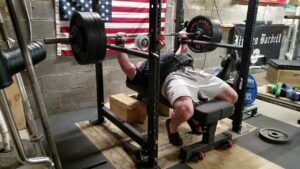 A man is lifting a barbell on a bench in a gym.