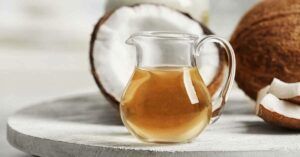 A pitcher of coconut oil is sitting on a table next to coconuts.