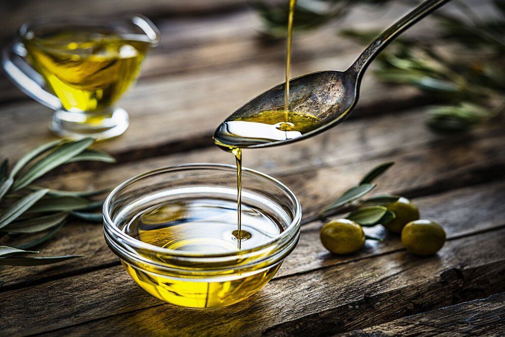 Olive oil is being poured from a spoon into a glass bowl.