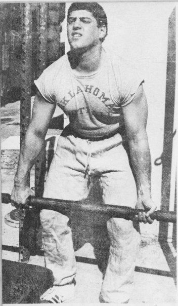 A man in an oklahoma shirt is lifting a barbell