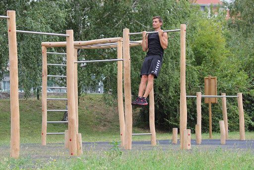 A man is doing pull ups on a wooden bar in a park.