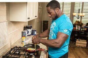 A man is cooking food in a pan on a stove in a kitchen.