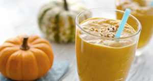 Two glasses of pumpkin smoothies with straws and pumpkins in the background.