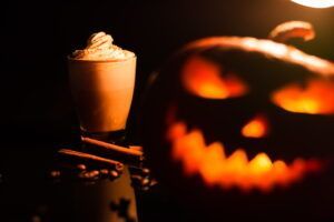 A cup of pumpkin spice latte next to a carved pumpkin.