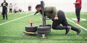 A man is pushing a sled on a football field.