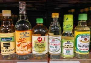 A variety of bottles of rice vinegar are lined up on a shelf.