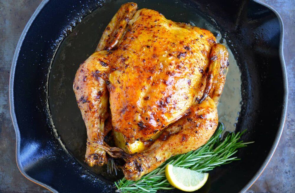 A roasted chicken in a skillet with lemon and rosemary.