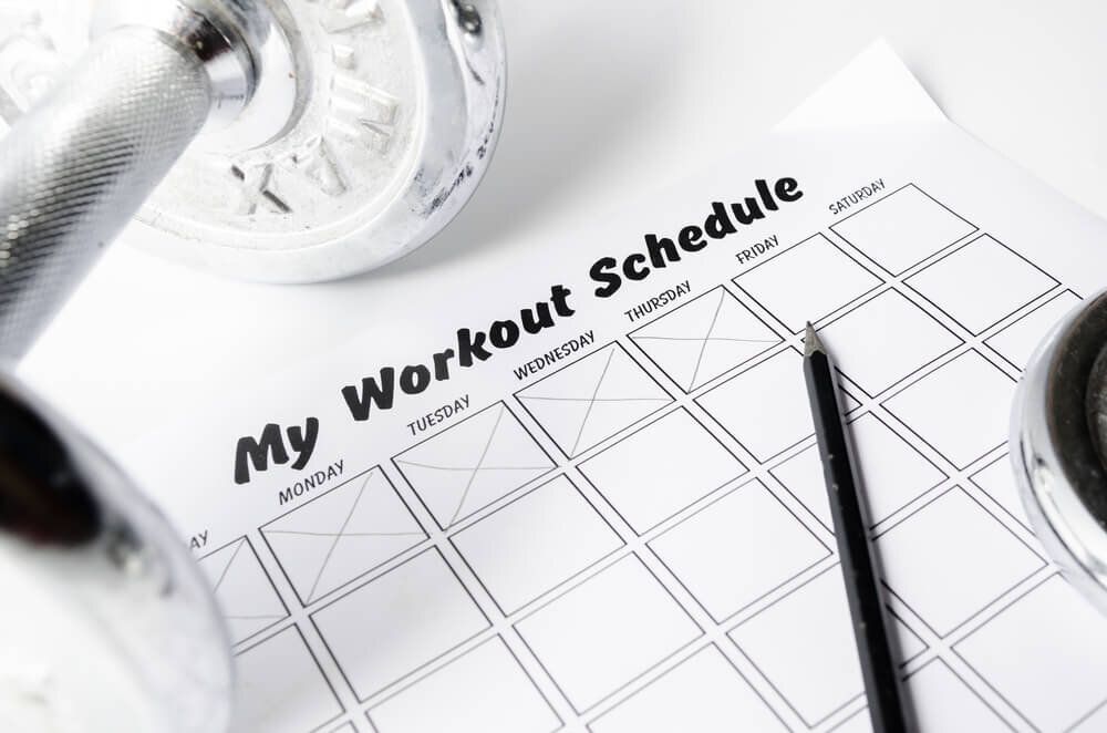 A workout schedule with dumbbells and a pencil on it