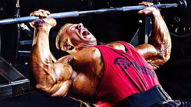 A man in a red tank top is lifting a barbell on a bench.